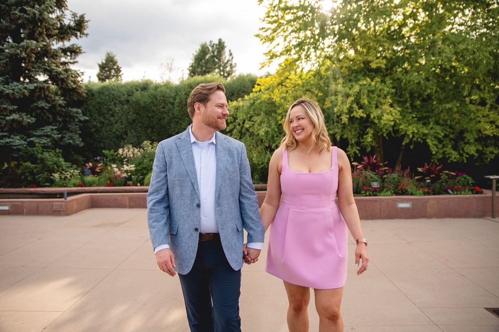 A couple strolls together through a scenic garden path wearing pink and blue coordinated outfits in summer.