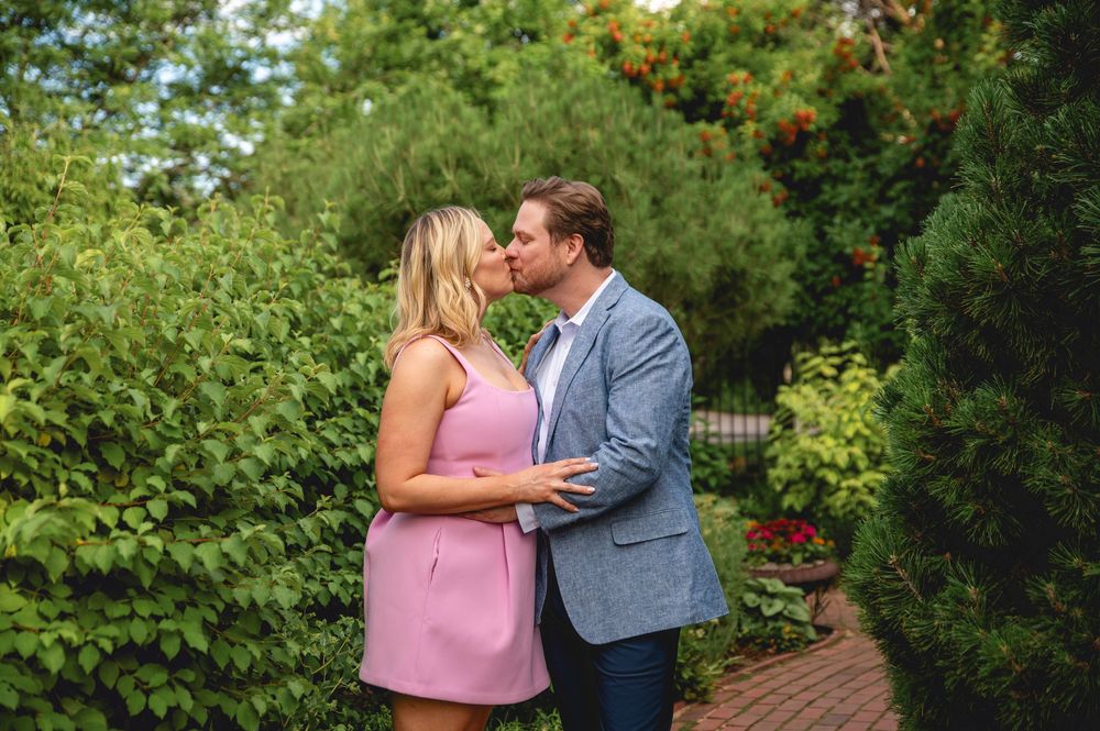 A couple shares romantic moments in a lush green garden setting during a photo session.