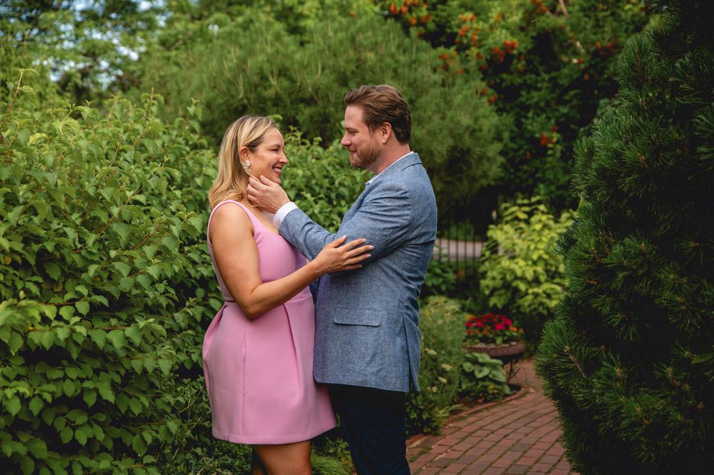 A couple shares a tender moment together on a garden pathway surrounded by lush greenery.