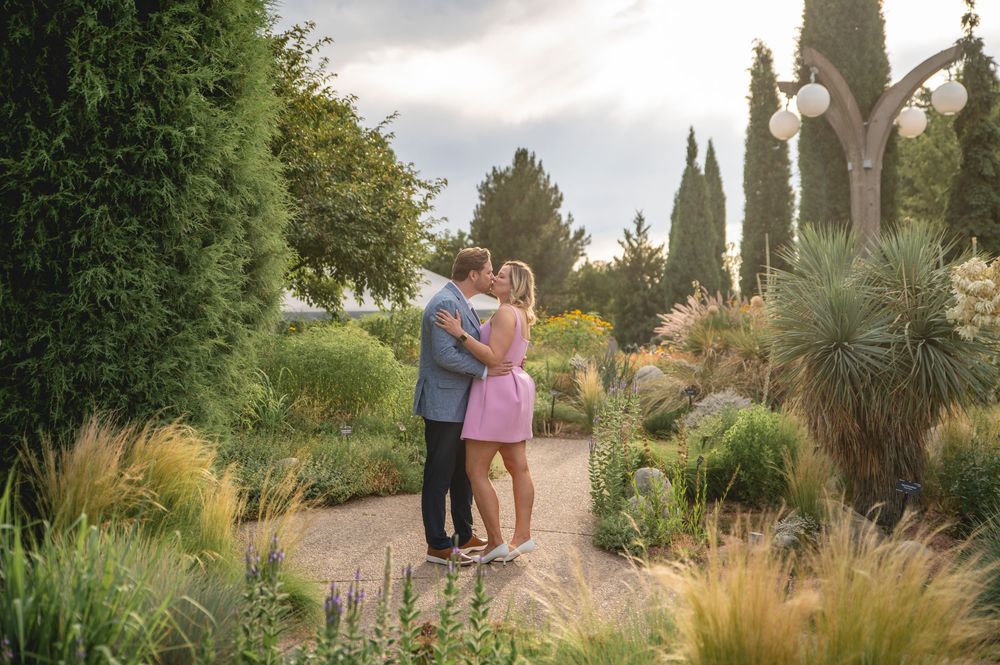 A couple walks along a garden path through ornamental grasses and landscaping at a scenic outdoor venue.