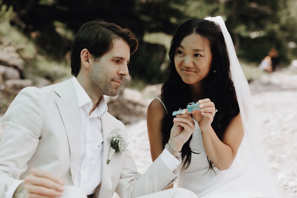 A joyful bride and groom share a candid moment together outdoors wearing white wedding attire.