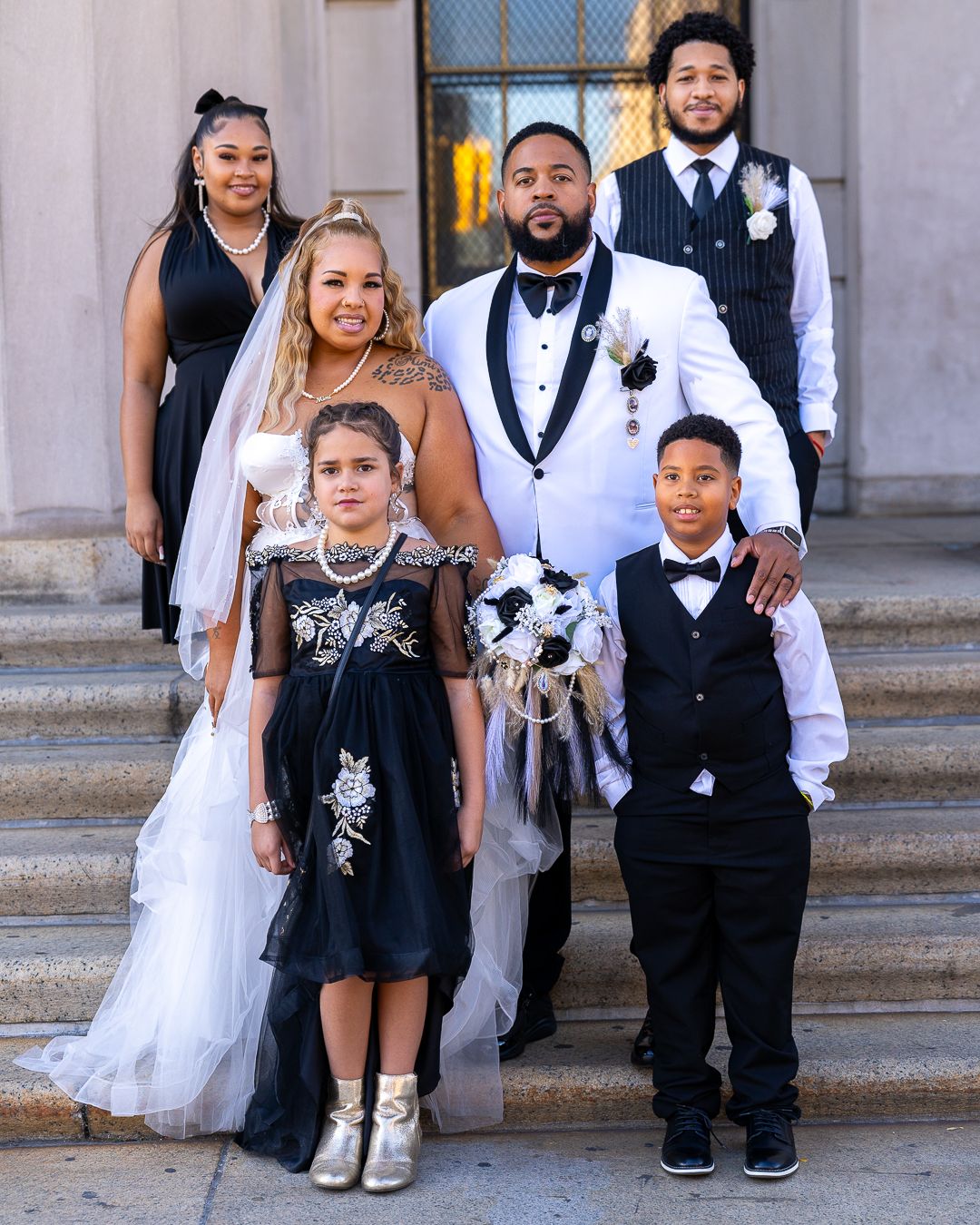 Wedding party poses on stone steps wearing elegant black and white formal attire for a celebration photo.