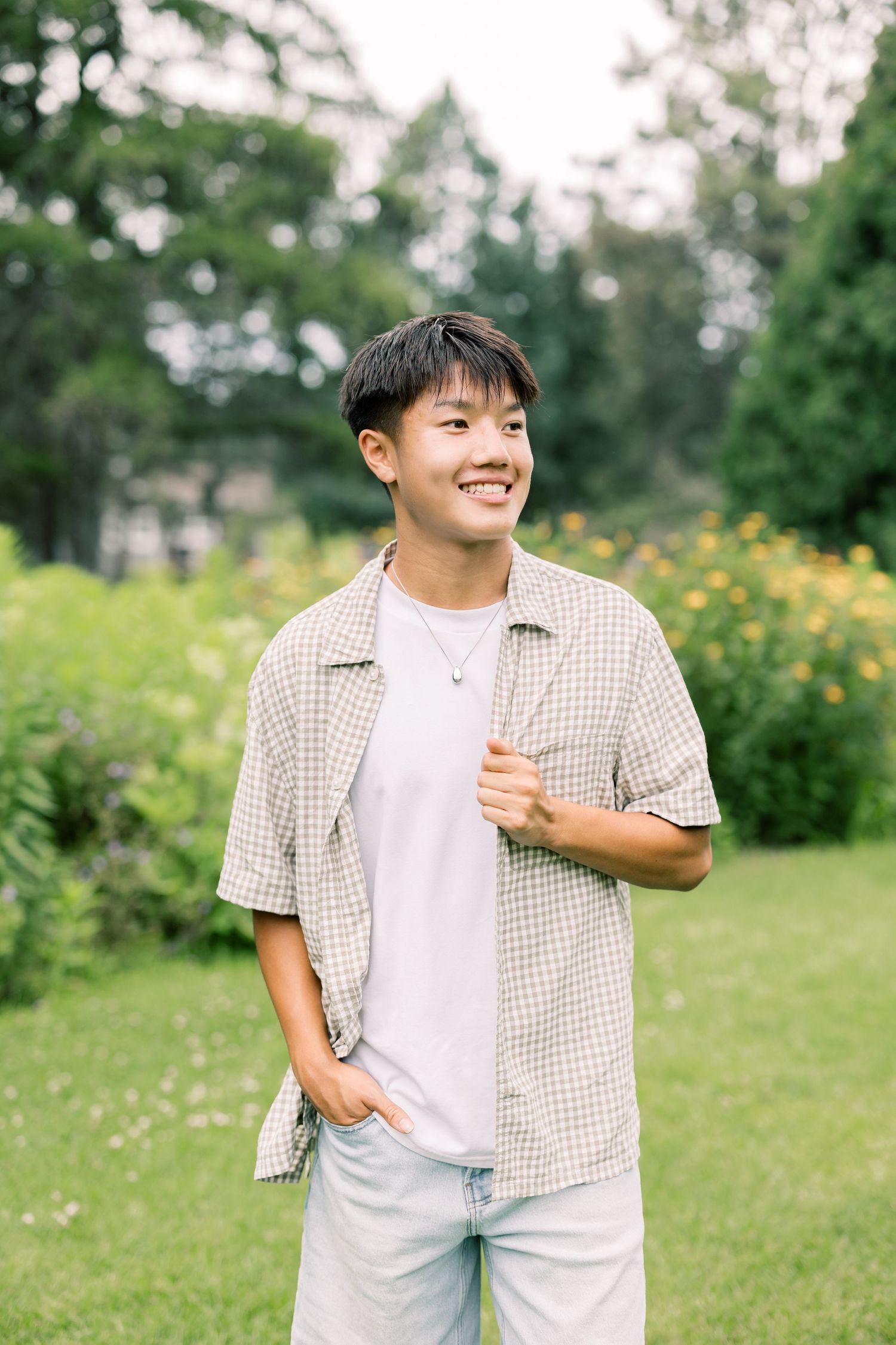 Person enjoying a sunny day outdoors wearing a checkered shirt and white t-shirt in a garden with yellow flowers.
