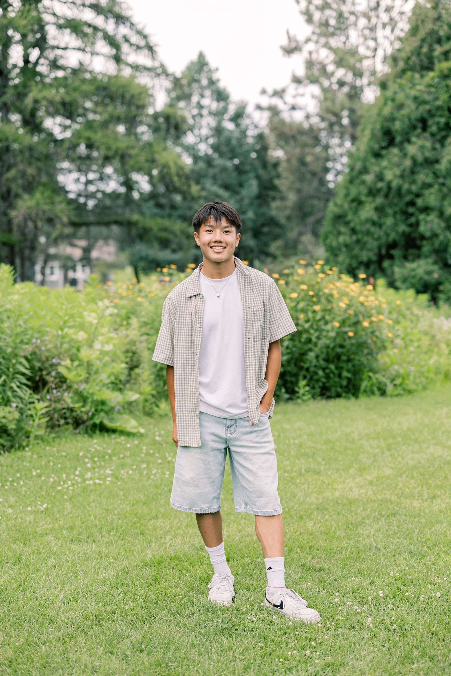 A child stands in a lush green field with yellow wildflowers wearing a light button-up shirt and shorts on a sunny day.