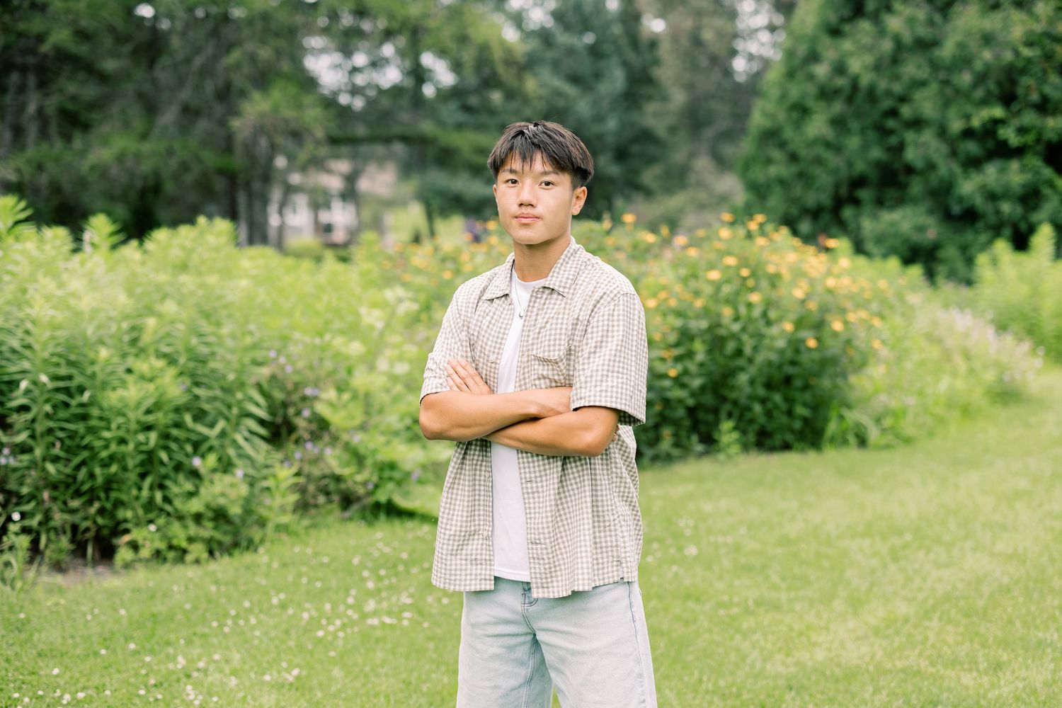 Person in light colored shirt standing in a garden with yellow wildflowers and green lawn on a sunny day.
