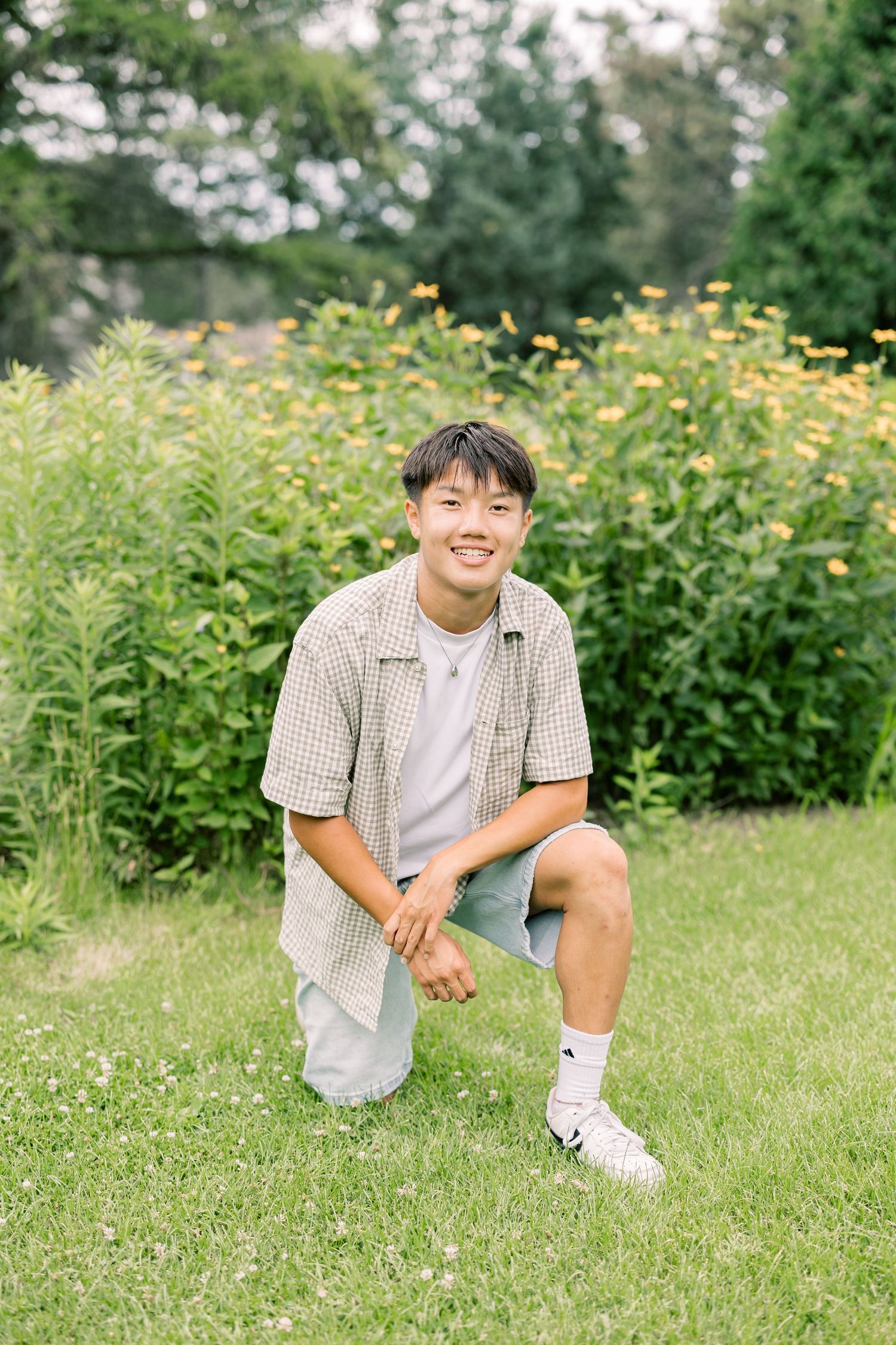 Person in checkered shirt sits casually on grassy field with yellow wildflowers blooming in background.