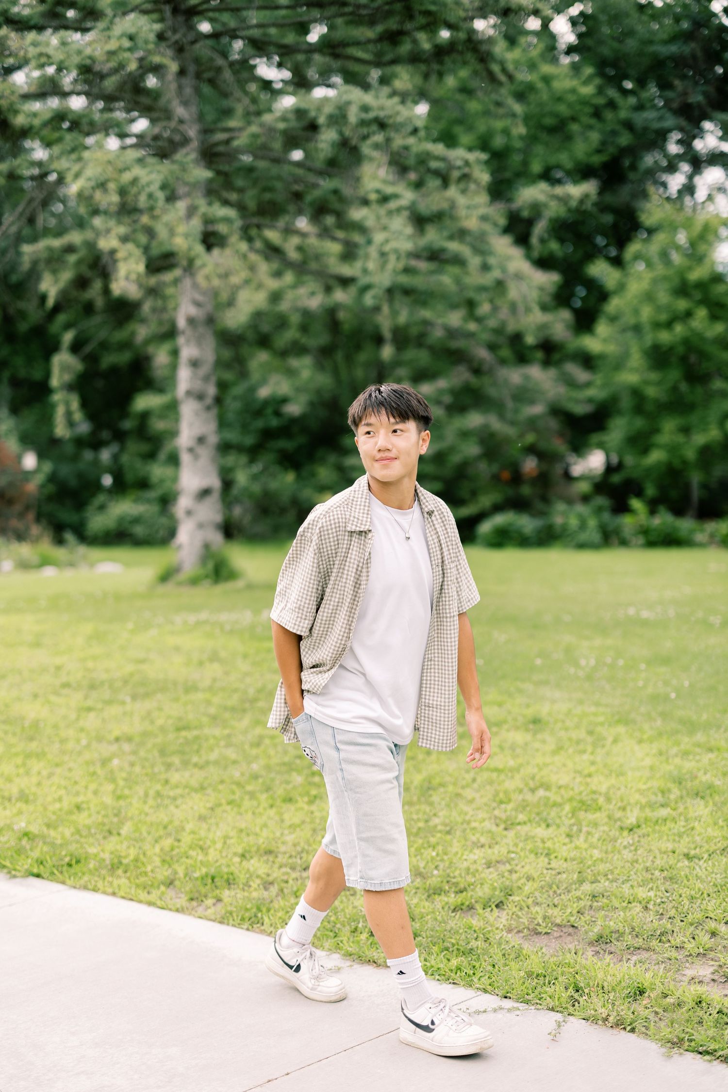 A young child wearing white clothing and sneakers walks on a pathway in a grassy park setting.
