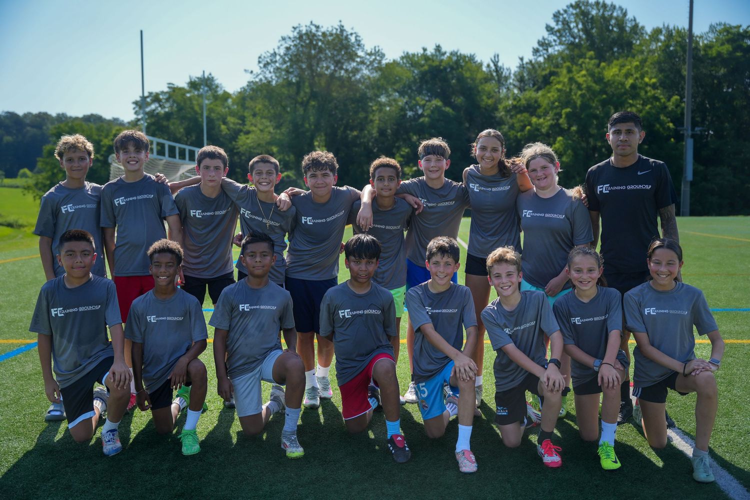 Youth soccer team in matching gray jerseys poses together on sunny field for team photo.