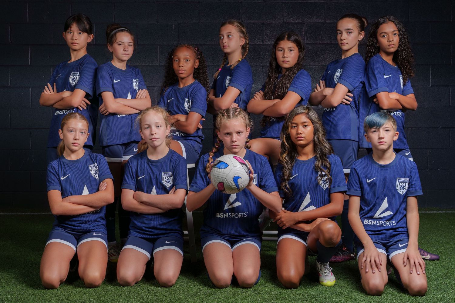 Youth soccer team in matching gray jerseys poses together on sunny field for team photo.