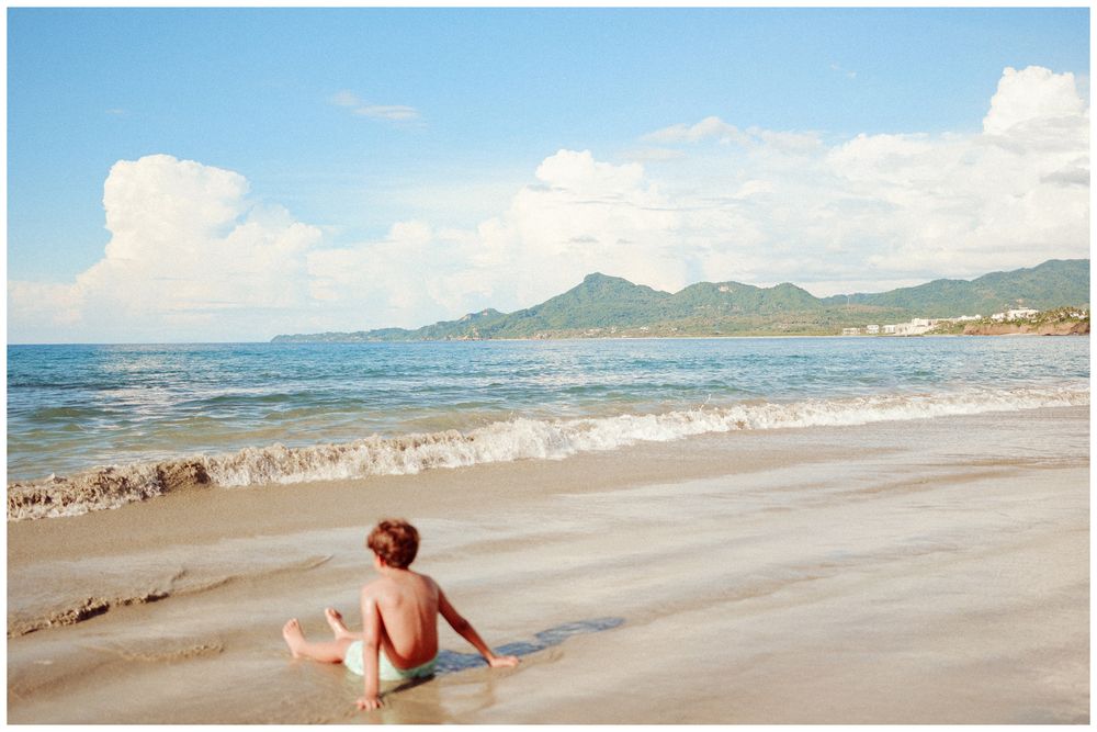 Panoramic view of a sandy beach with mountains in the distance showing waves rolling onto the shoreline.