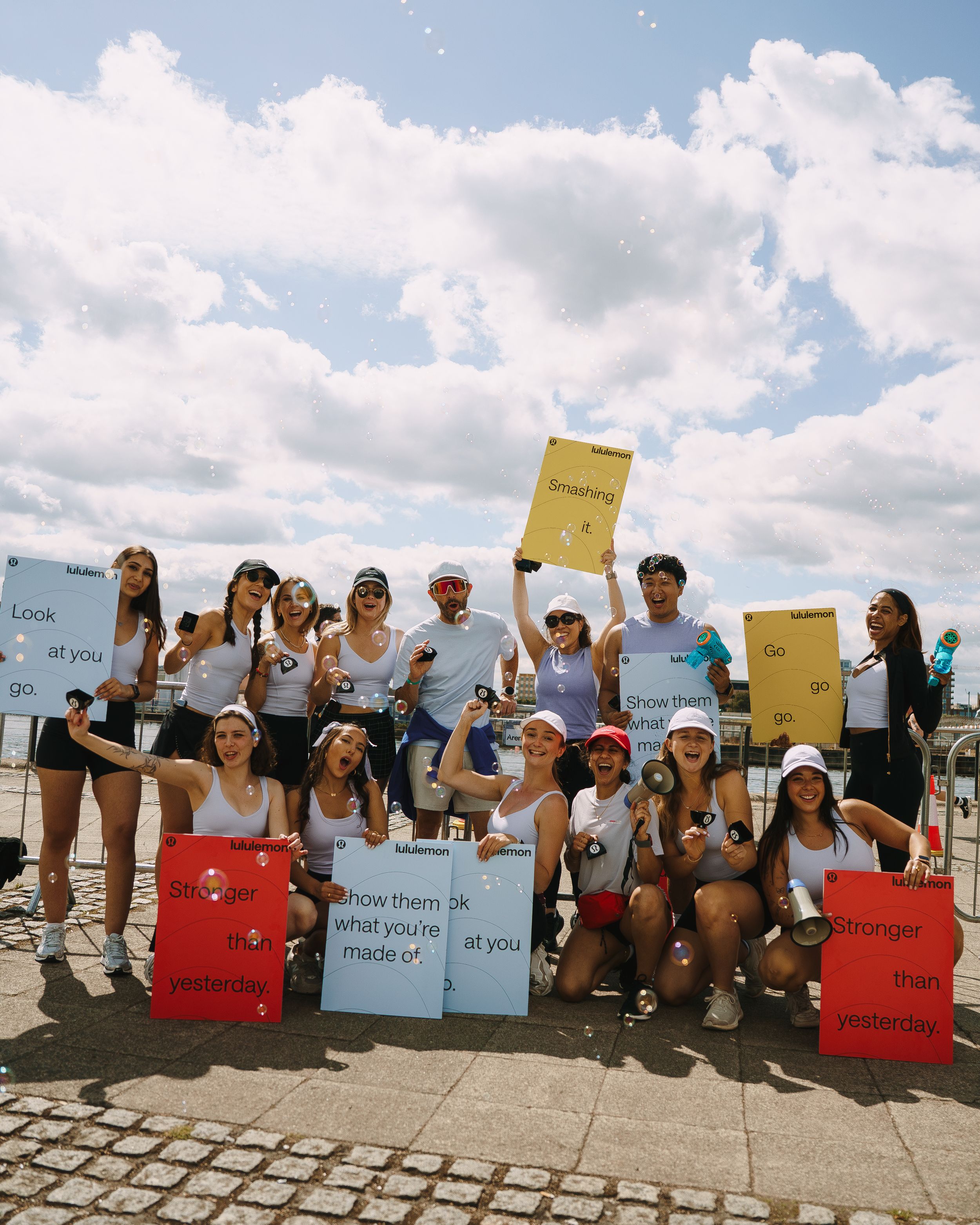 A group of people sitting on a stone wall holding colorful protest signs during a sunny day.