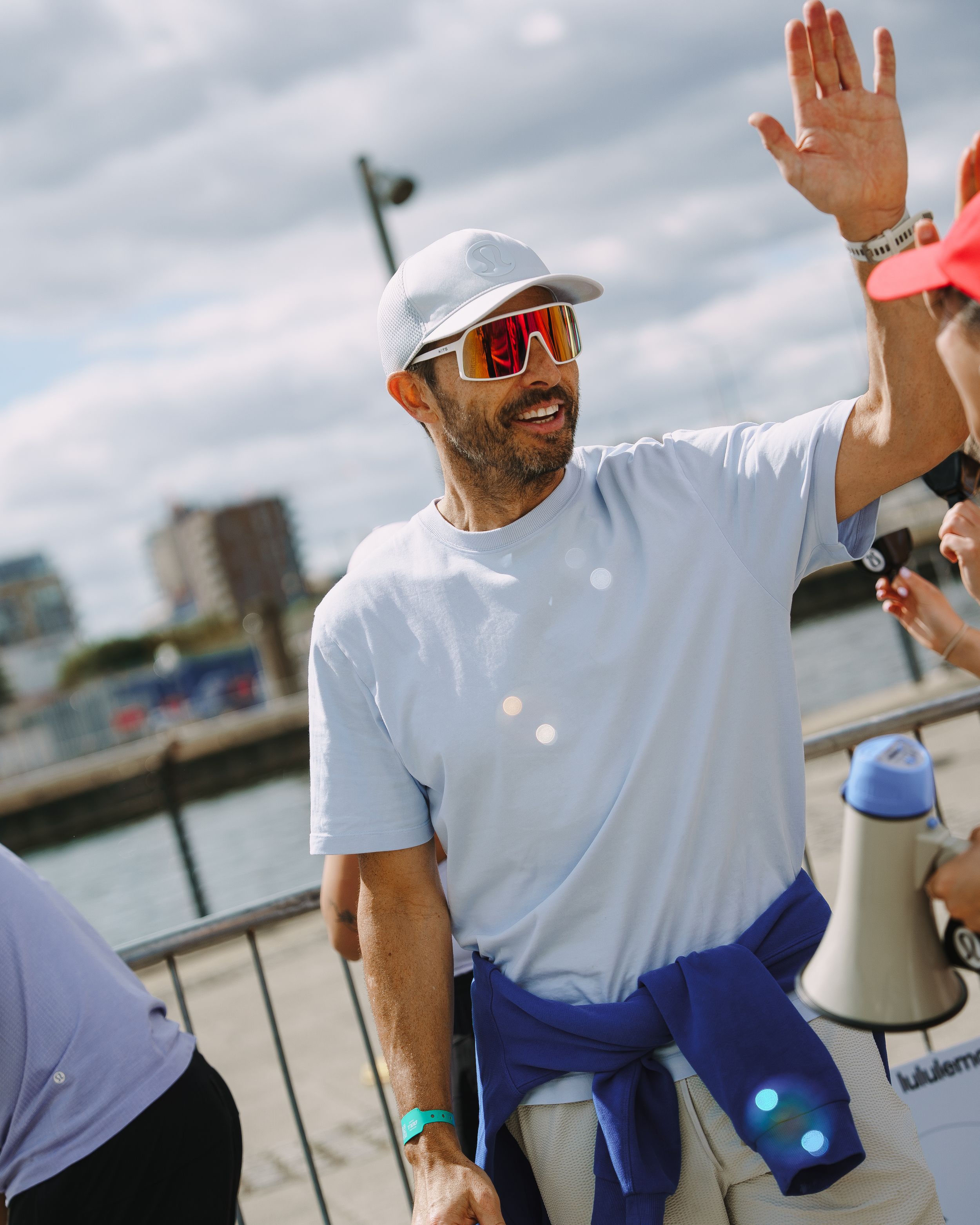 Person in white t-shirt and blue shorts waving and smiling during outdoor activity.