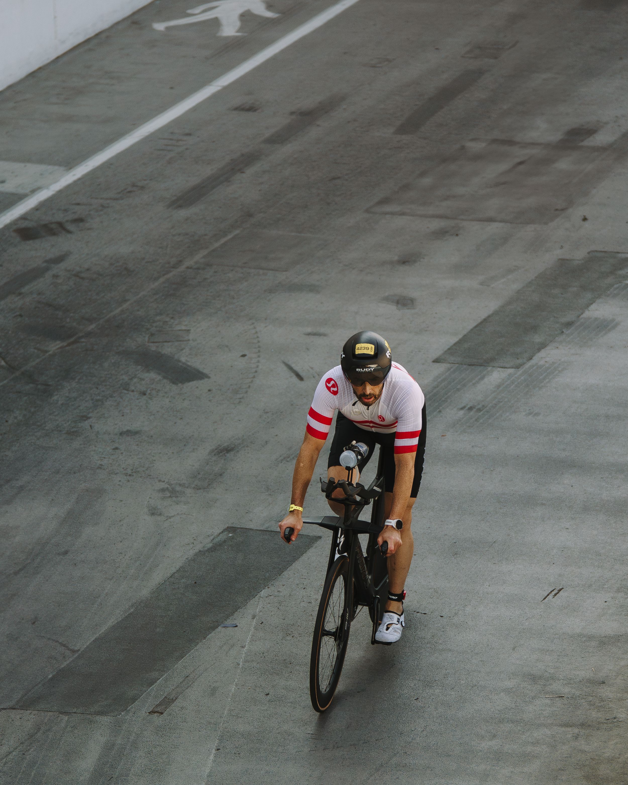 Cyclist in red and white jersey racing on an indoor track with painted markings.