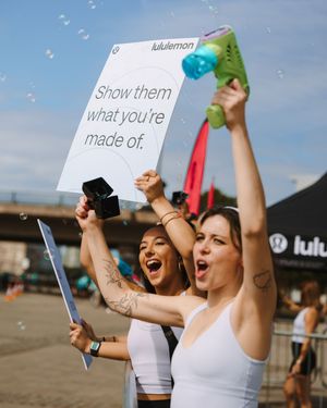 A group of enthusiastic people in white tank tops raise signs and cheer during an outdoor event.