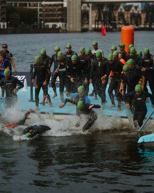 Athletes in green swim caps and wetsuits dive into the water at the start of a triathlon race.