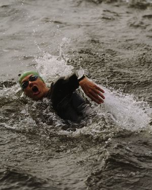 Swimmer in green swim cap splashing through muddy water during an outdoor competition.