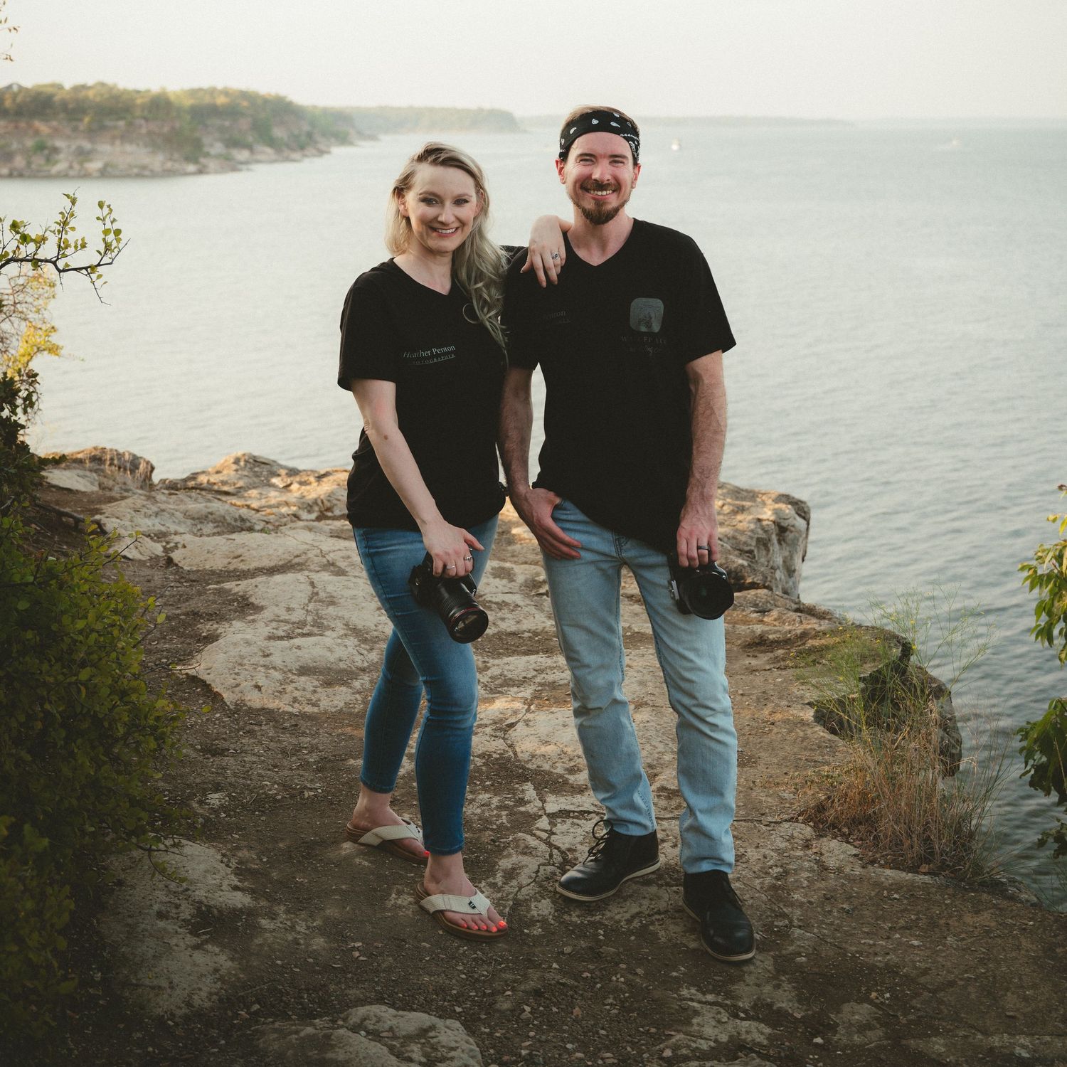 A couple (Jon and Heather Photographers Team) sits together on a rocky coastal overlook with a scenic ocean view in the background.