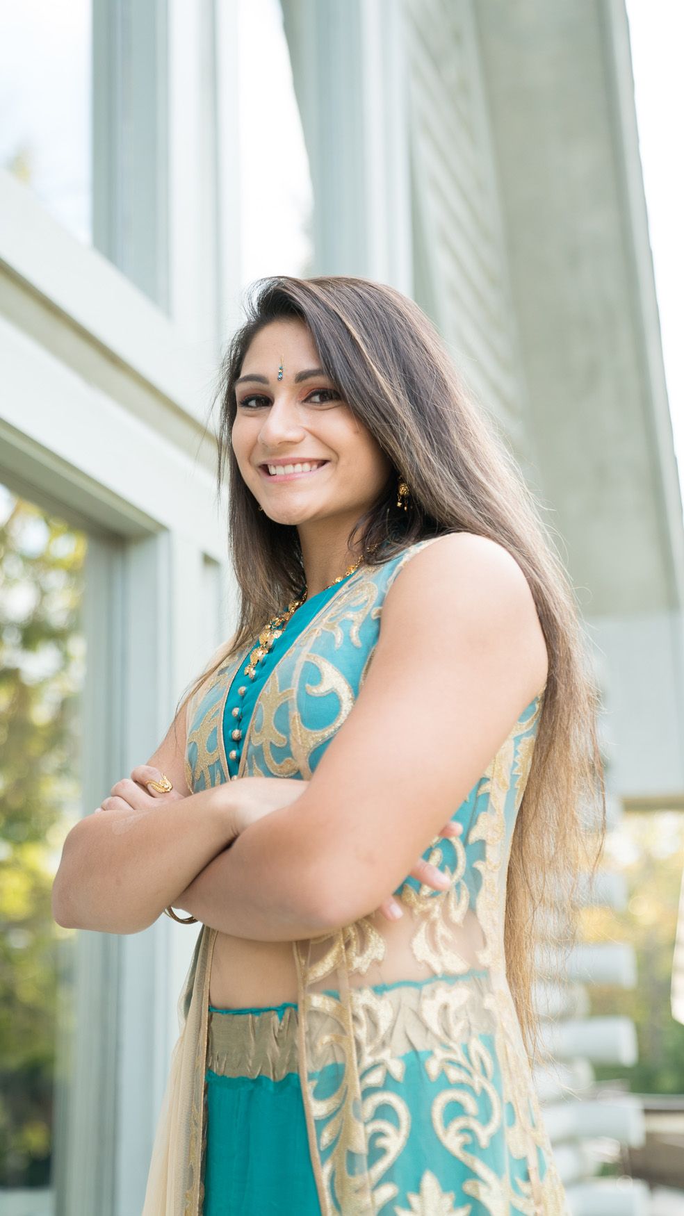 A portrait series of a woman wearing a turquoise and beige patterned top posing against a bright exterior wall.