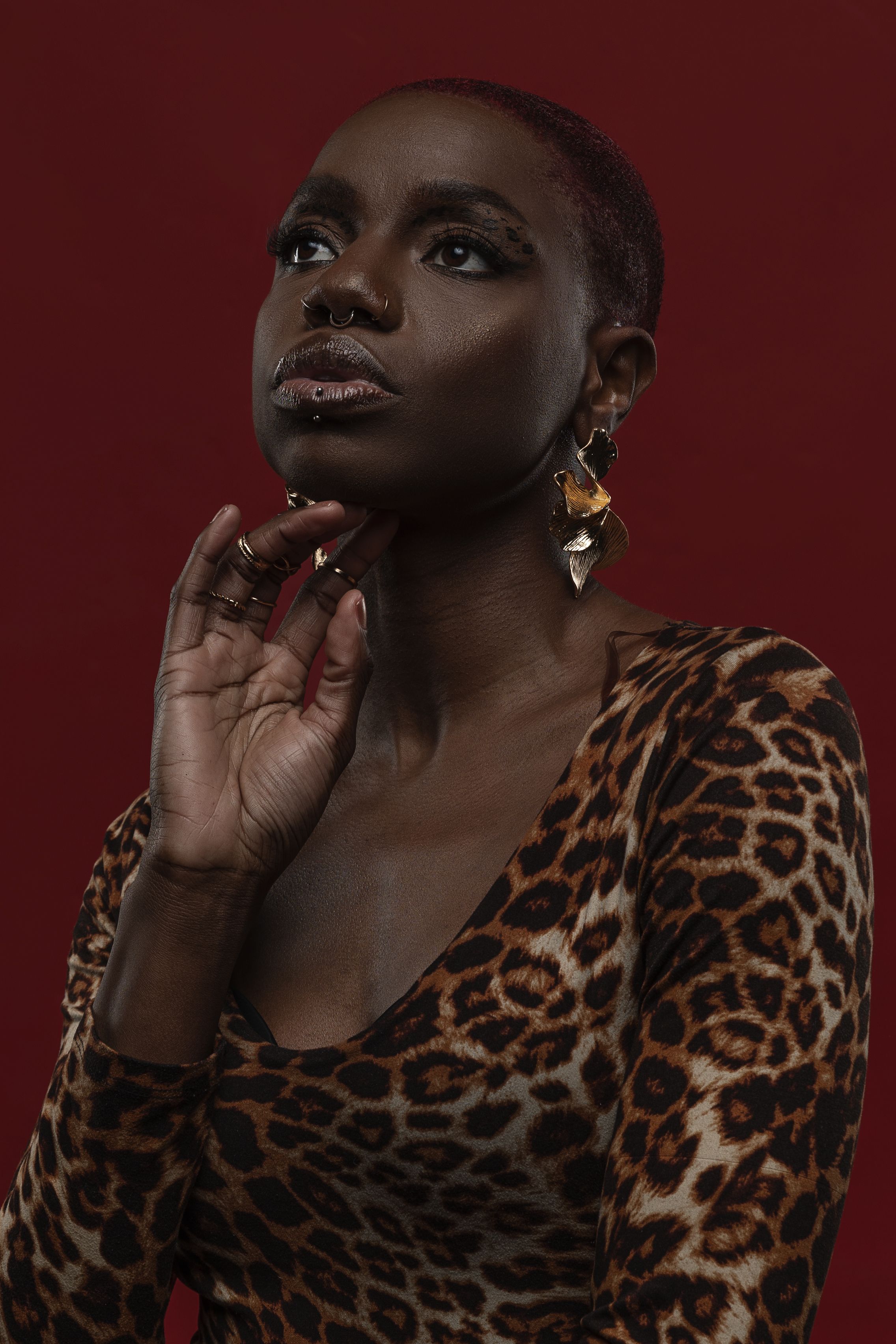 Model in leopard print top poses expressively against dark burgundy backdrop in artistic portrait series.
