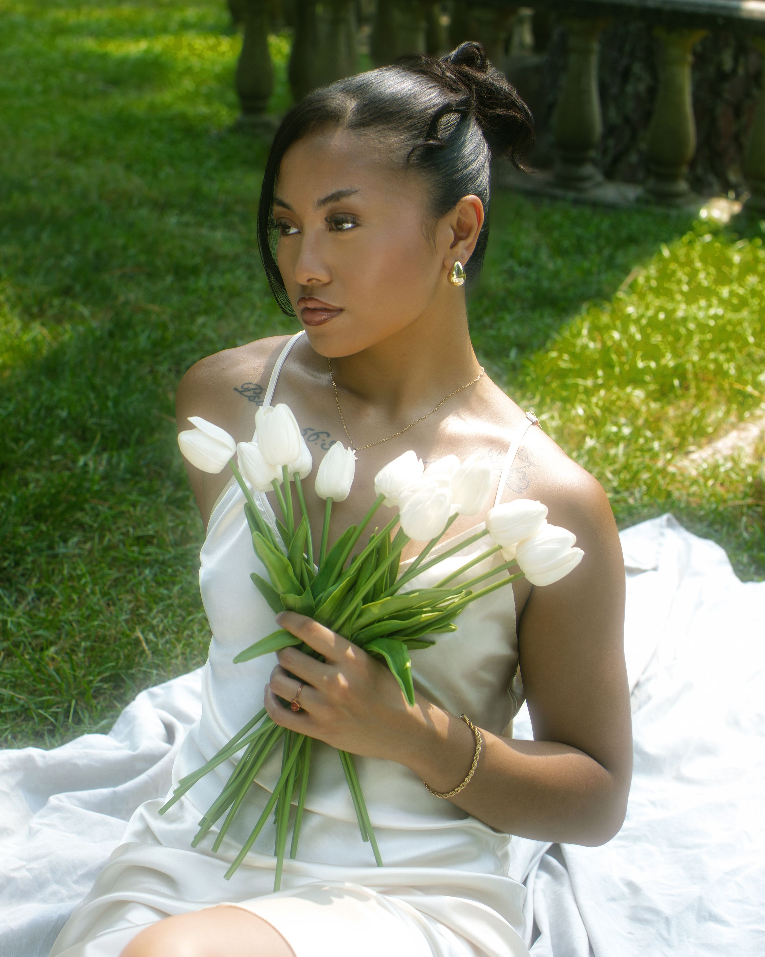 Bride wearing flowing white wedding dress poses with delicate white tulips in a sunlit garden setting.