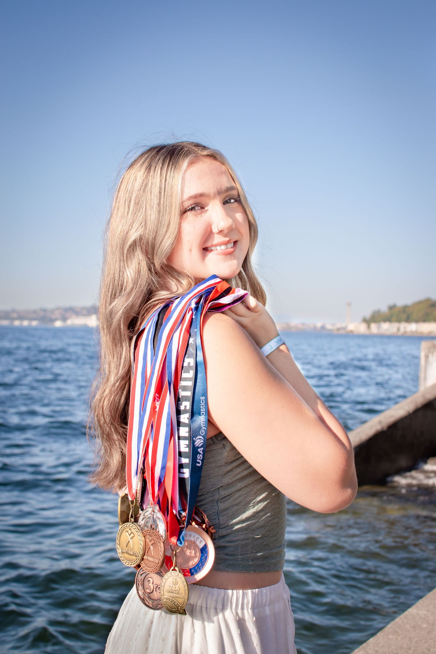 Seattle senior girl proudly posing with gymnastics medals at Alki Beach during graduation portraits.