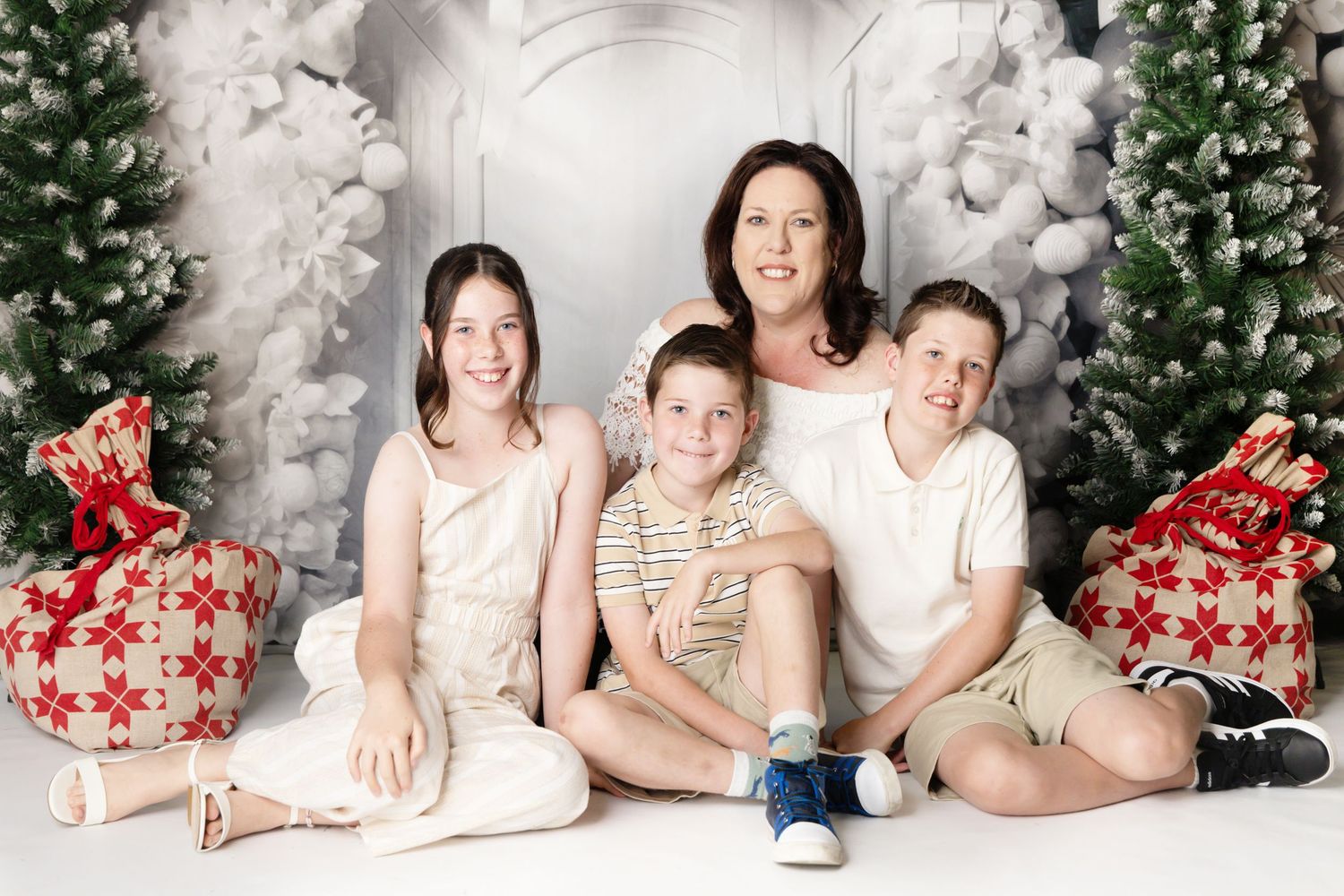 Four children in red holiday shirts sit together on white Christmas steps surrounded by winter decorations.
