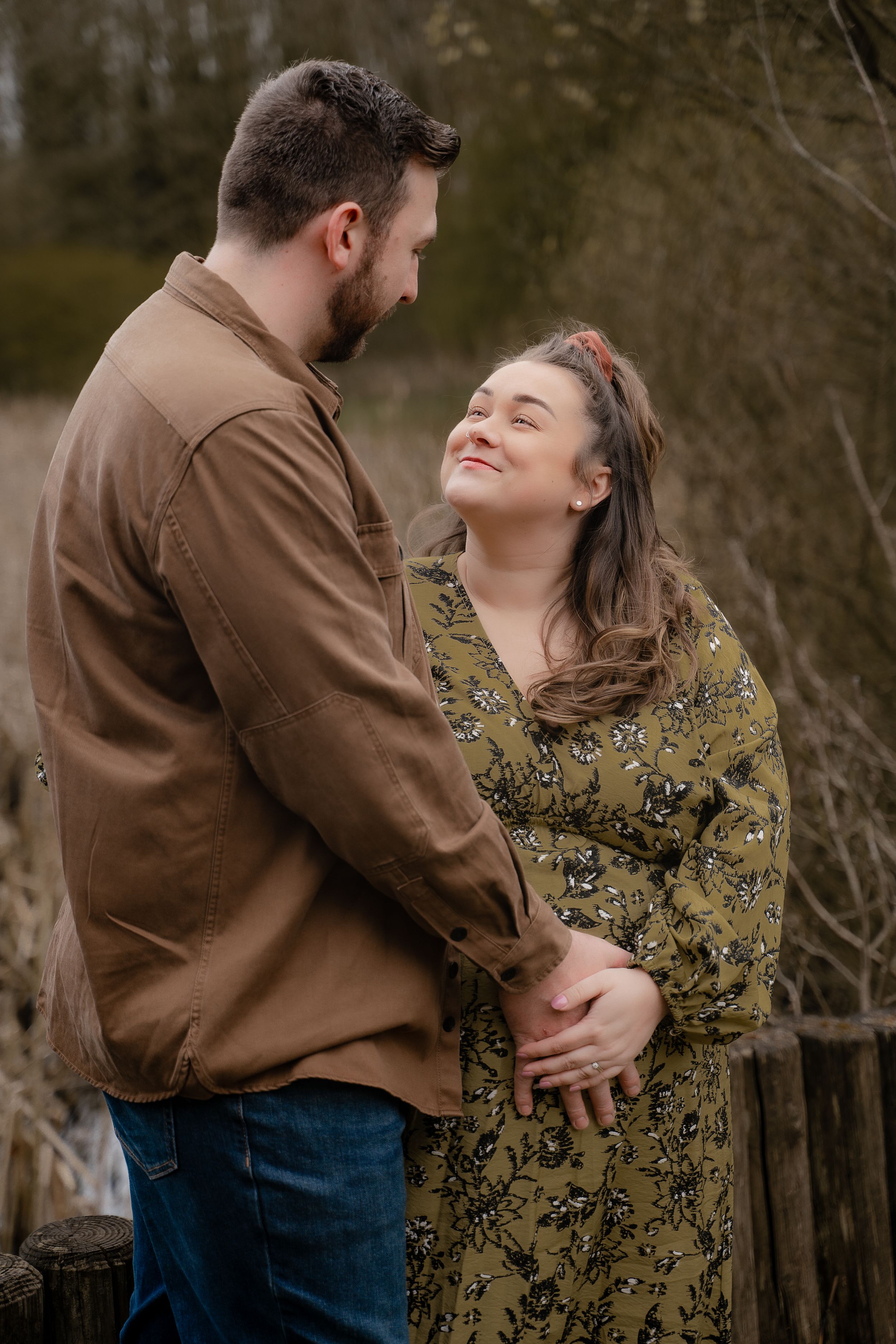 A couple embraces intimately in an outdoor setting wearing brown and floral outfits in a romantic photoshoot series.