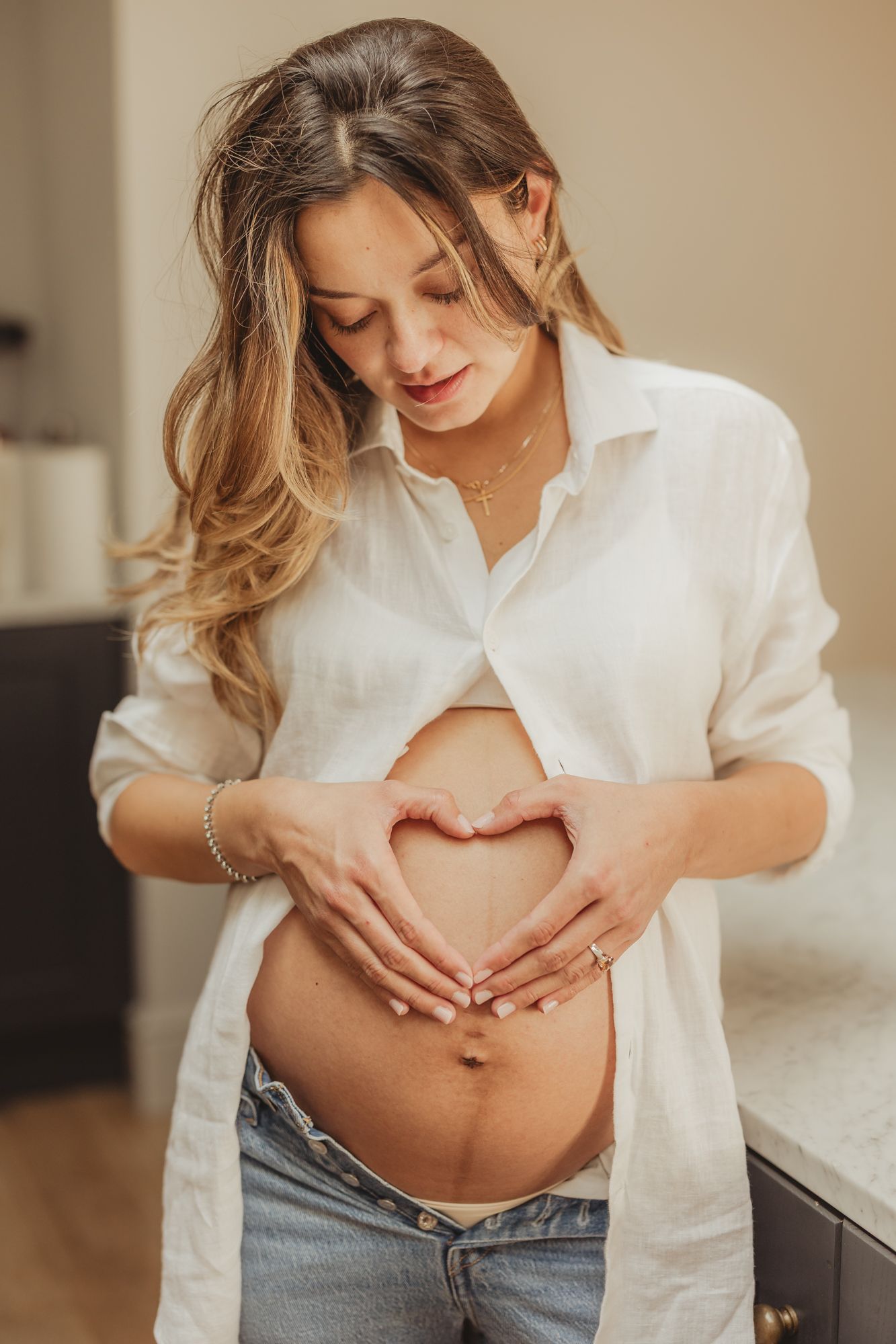 A series of photos showing a pregnant belly in a white button-down shirt and jeans against a warm indoor backdrop.