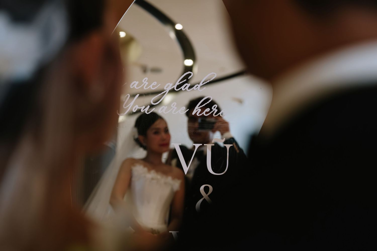 Artistic wedding photo captured through mirror reflection showing bride and groom with VU monogram overlay.