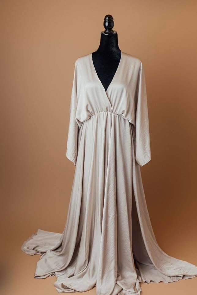 Flowy cream-colored empire waist dress with long sleeves displayed on mannequin against brown backdrop.
