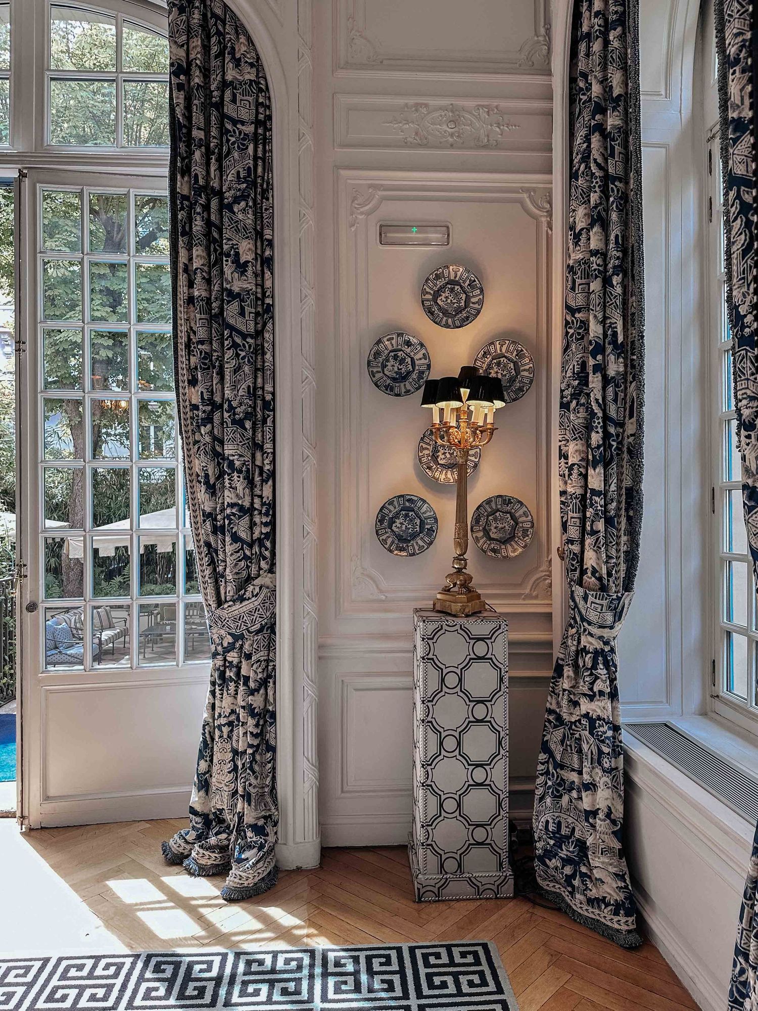 Elegant corner with black and white floral curtains, decorative wall plates, and a Greek key pattern rug in a period room.