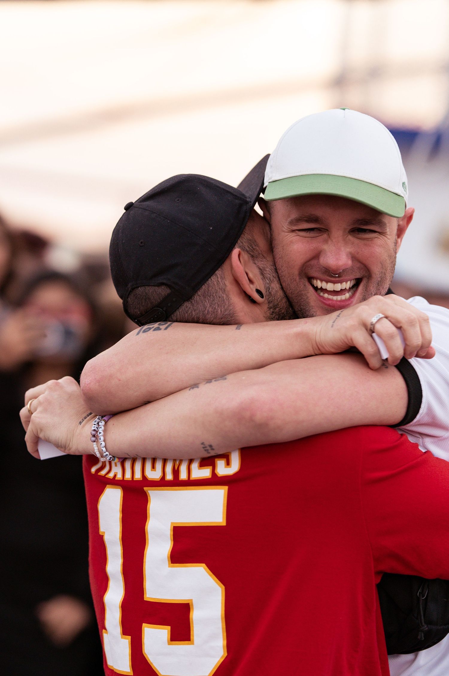 Two sports fans share joyful embrace, one wearing Chiefs jersey number 15.