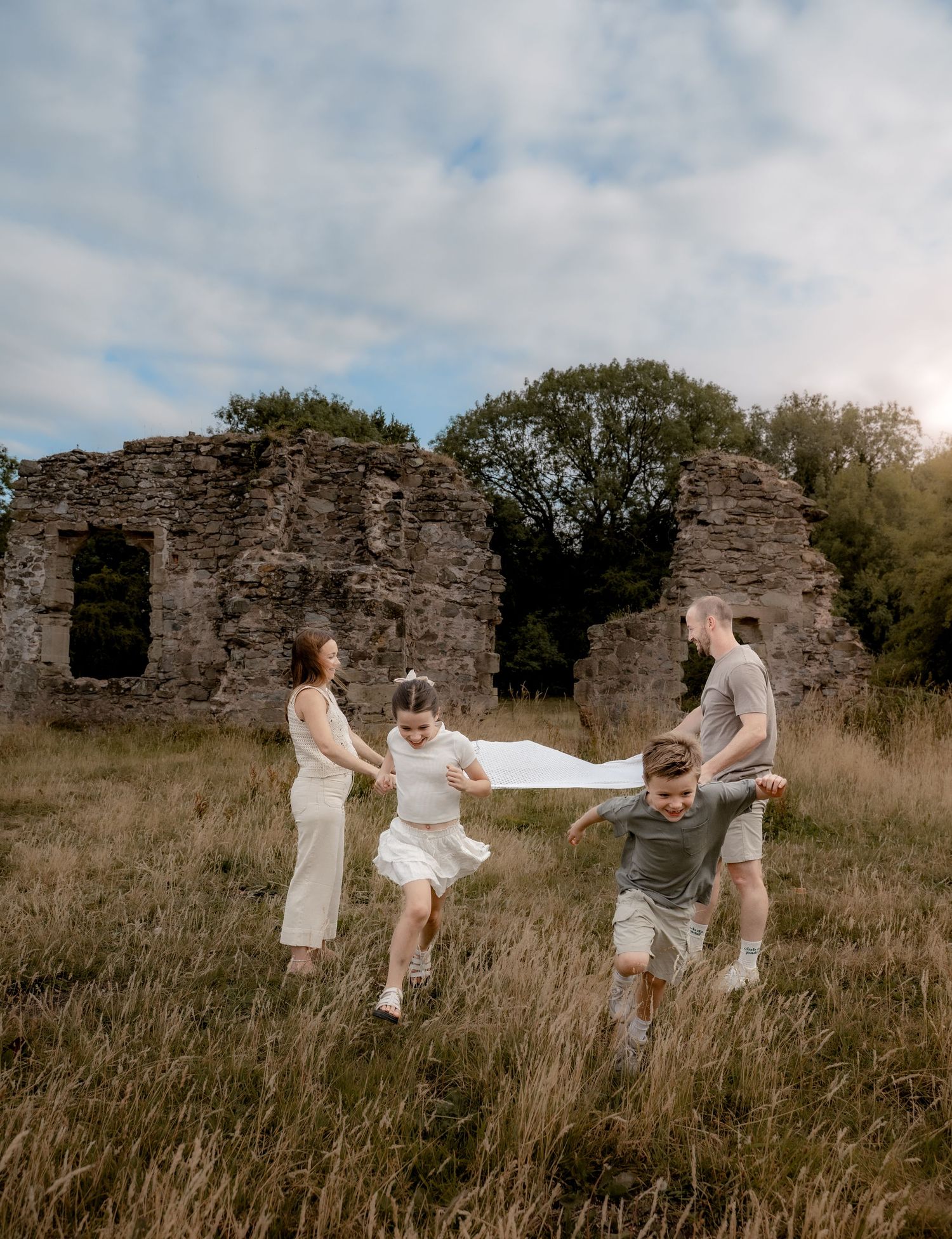 Four children run joyfully toward the camera through a sunlit field with ruins in the background. A vibrant, candid storytelling photo