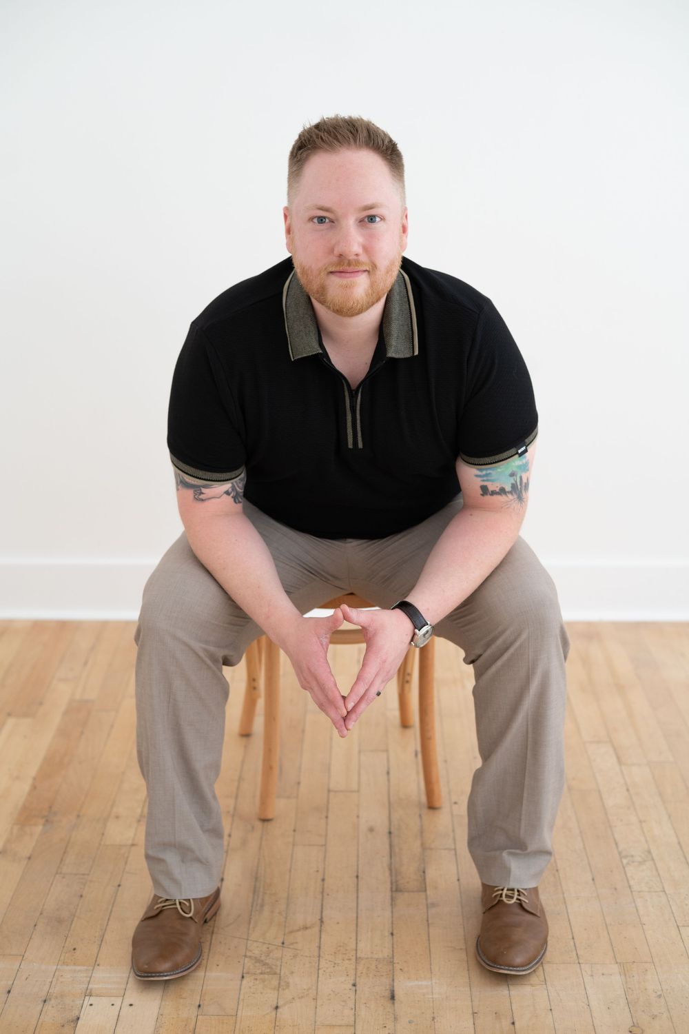 Person in casual attire sitting on wooden stool against white wall.