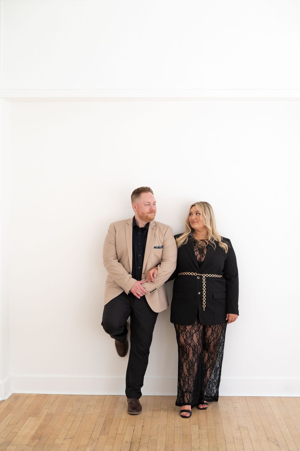 A couple posing against a white wall wearing formal attire.