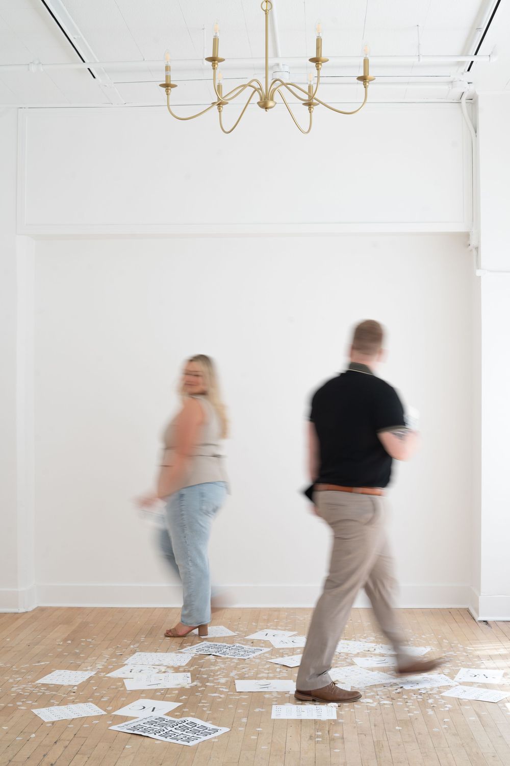 Blurred motion of people moving in white room with chandelier and scattered papers.