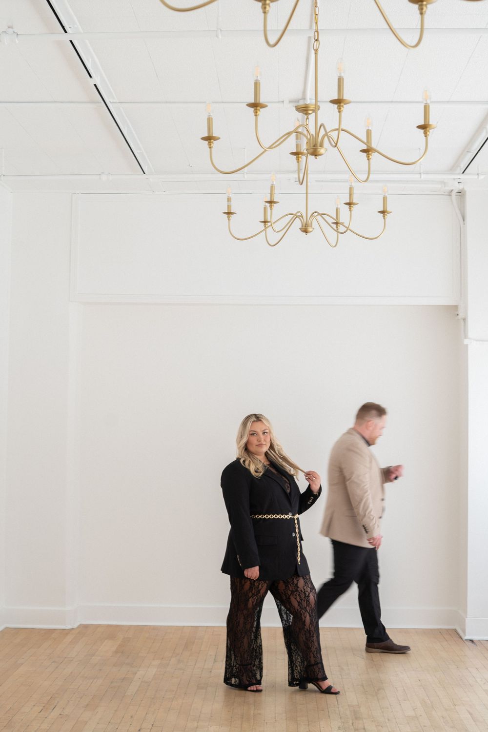 Two people standing in a white room with an elegant gold chandelier overhead.