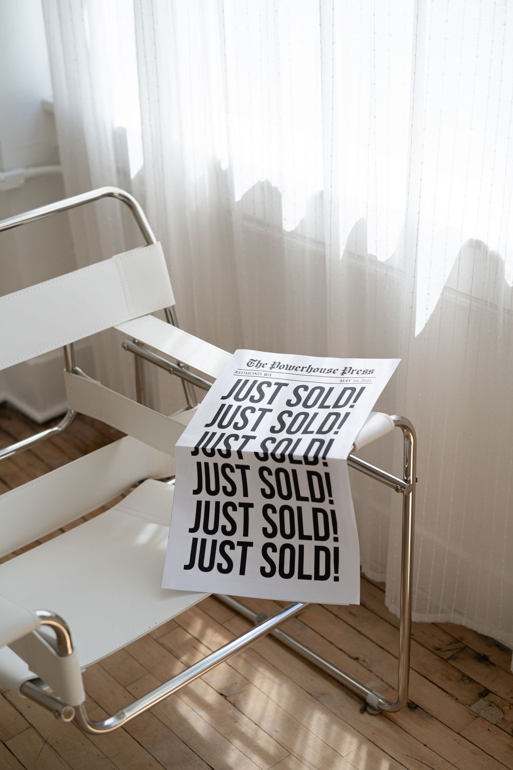 Multiple 'JUST SOLD' signs stacked on a white chair near a window with sheer curtains.