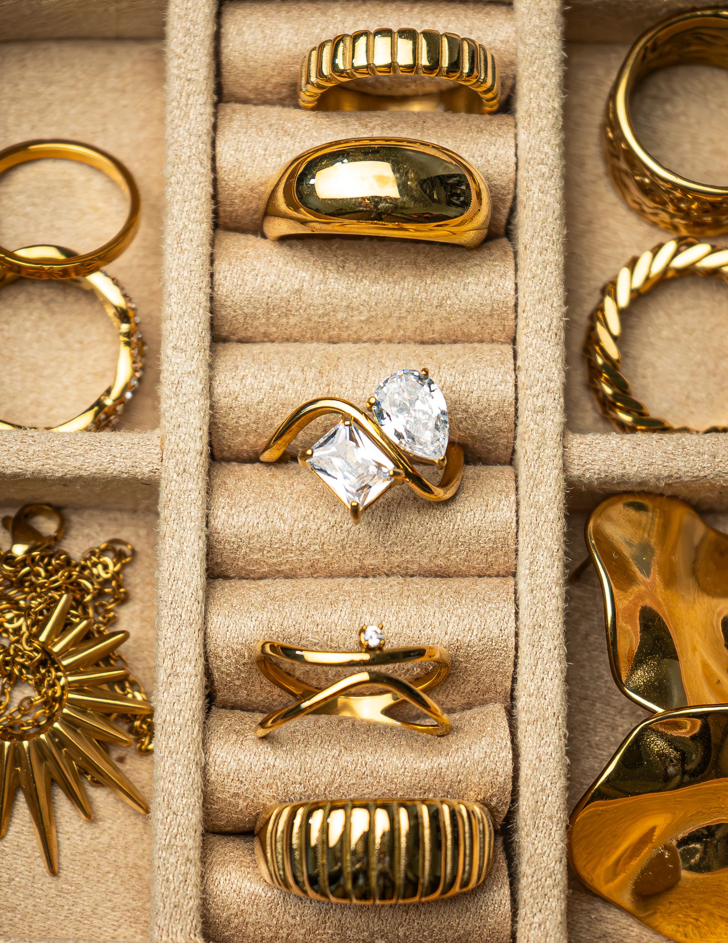 Assorted gold rings and jewelry organized in a beige jewelry tray.