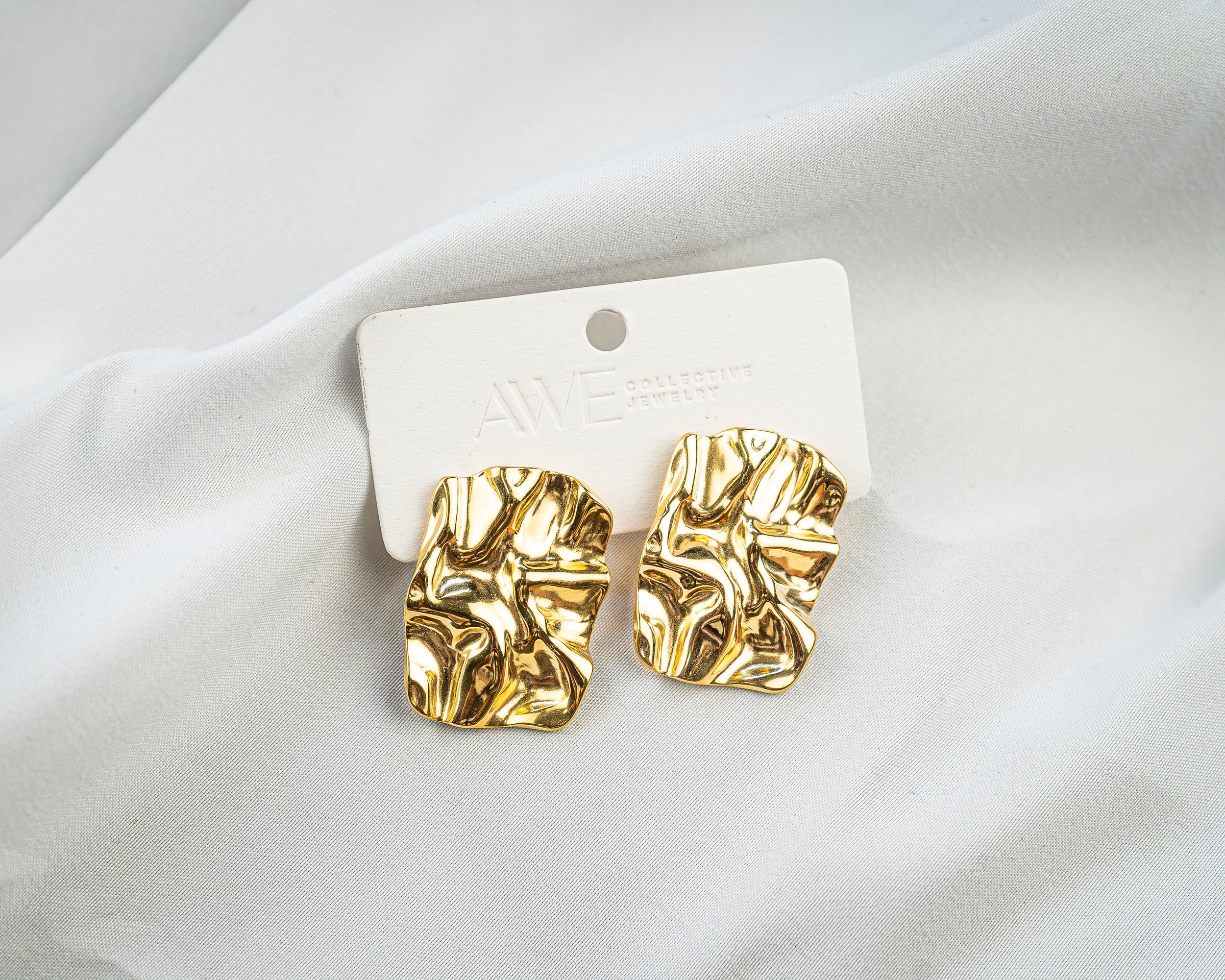 Pair of textured gold earrings on a display card over white fabric.