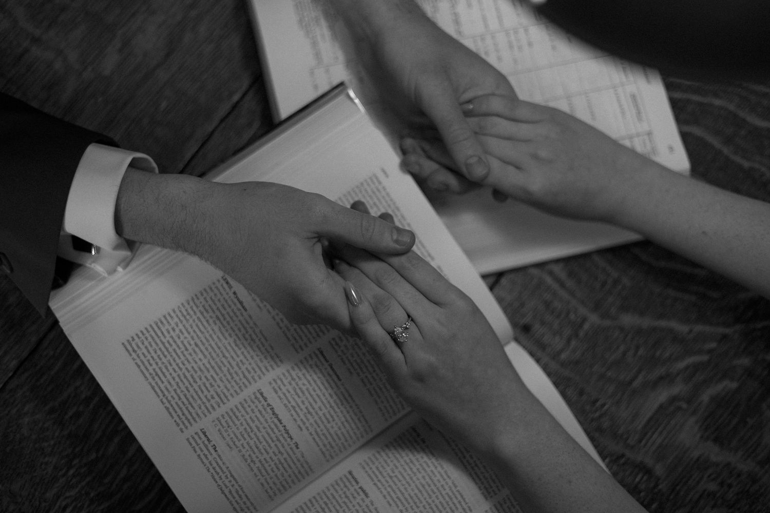 Black and white photo of hands touching tenderly across an open book page.
