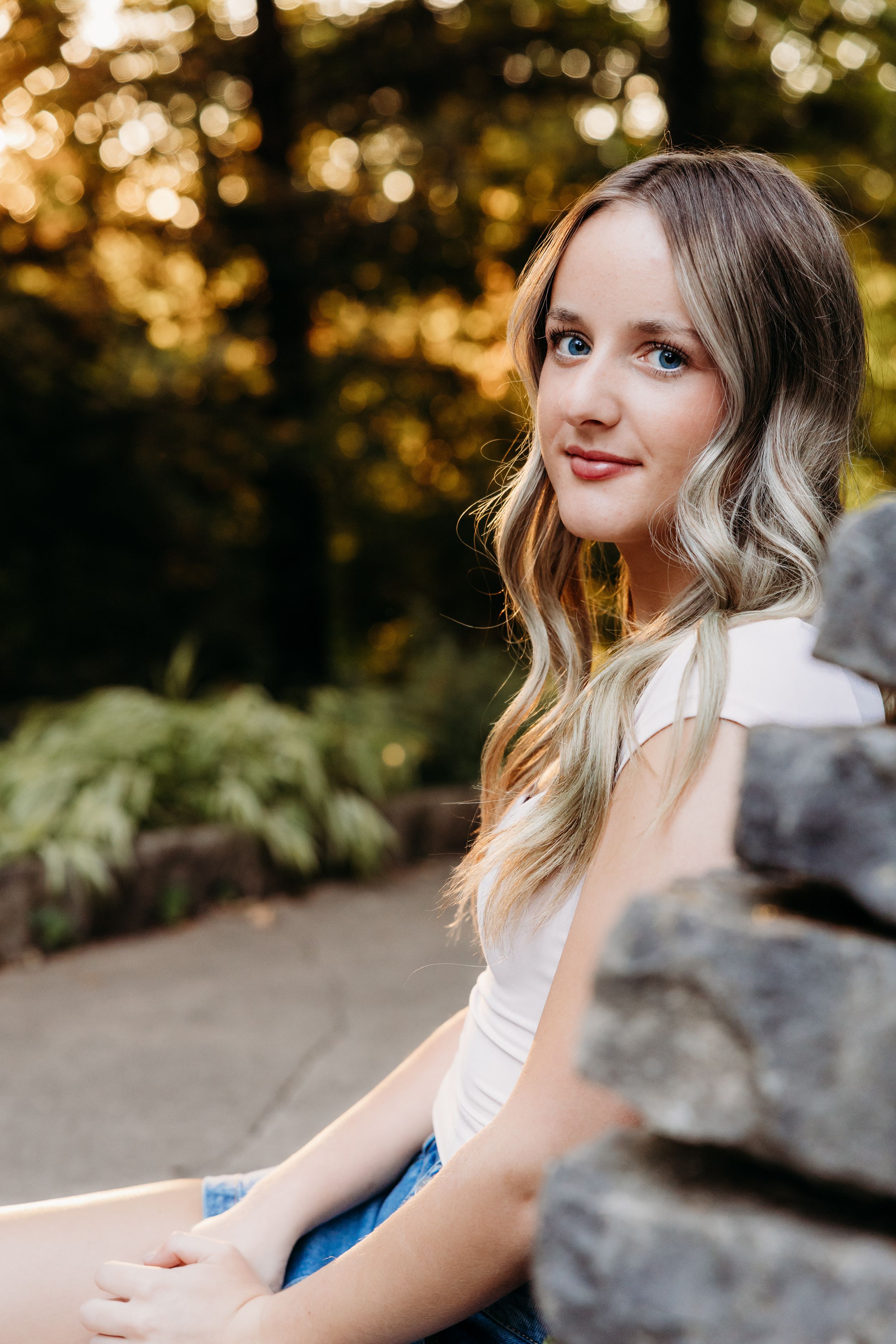Portrait shot in soft natural lighting with blurred autumn foliage background and stone wall details.