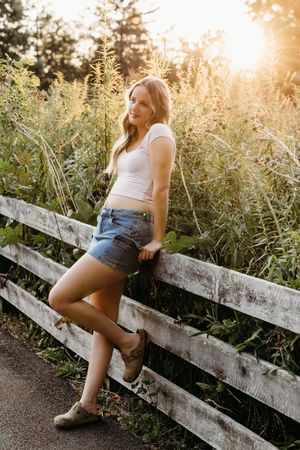 Sun-drenched portrait of someone sitting on a rustic wooden fence surrounded by tall wildflowers at golden hour.