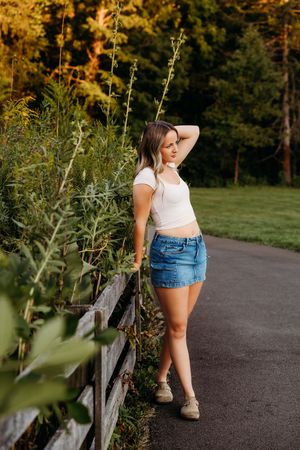 Summer outdoor portrait along rustic fence with golden sunset light illuminating lush greenery and paved path.