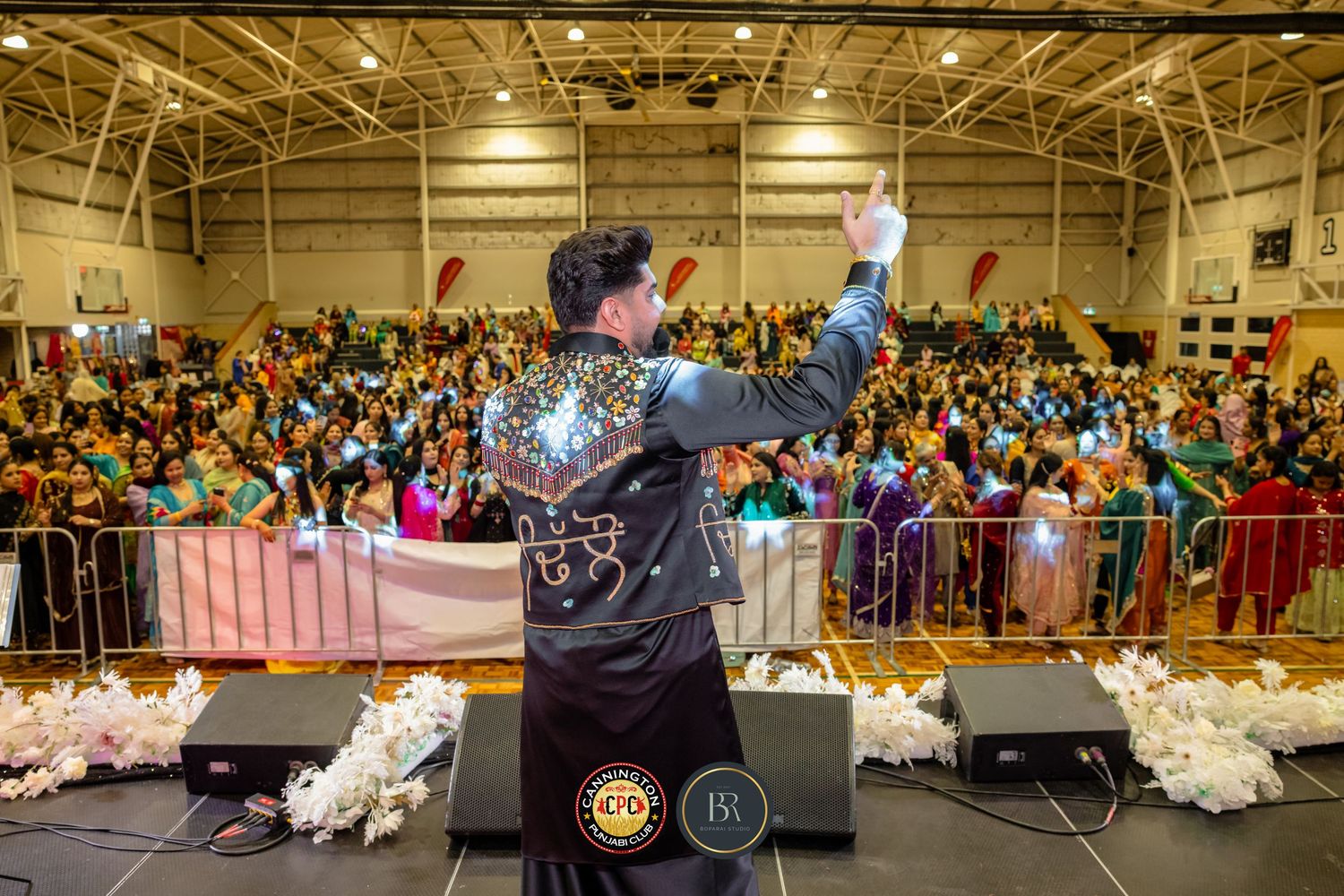 Panoramic view of a large indoor event with a stage and crowded audience in a brightly lit hall.