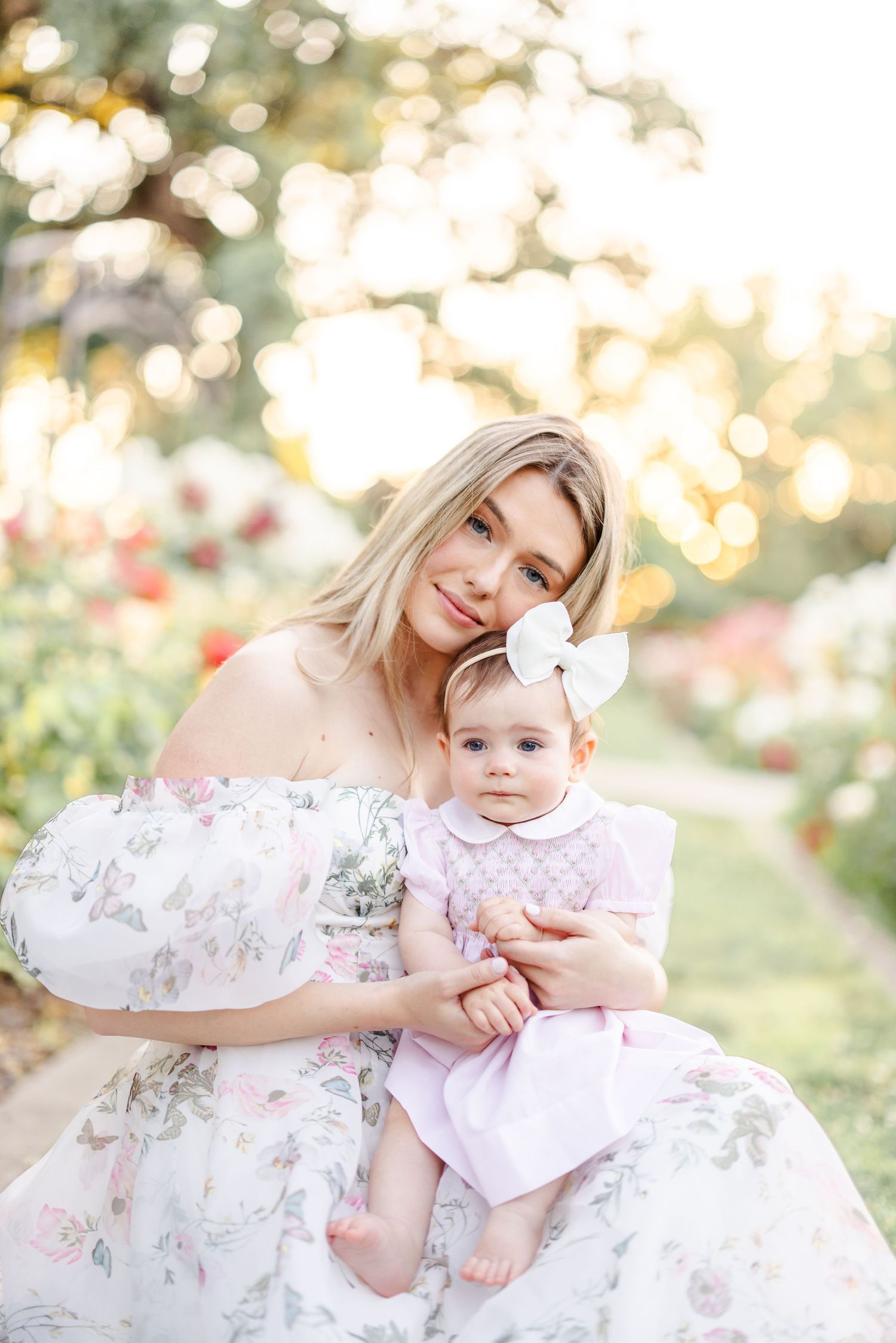 A tender moment between parent and baby wearing matching floral dresses in a sunlit garden.
