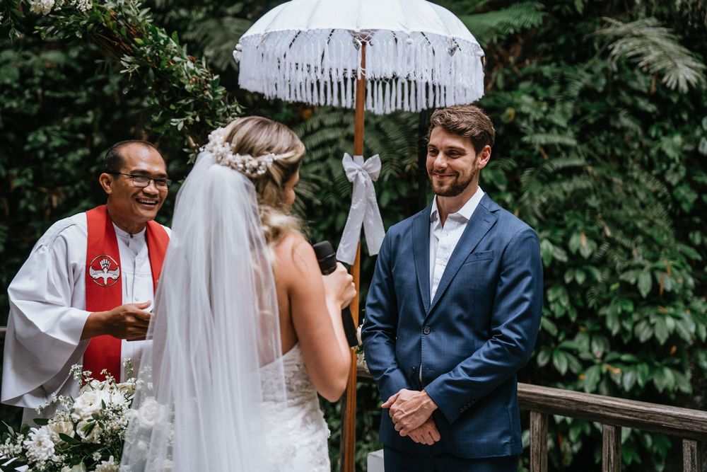 A wedding ceremony in progress under white decorative umbrellas surrounded by greenery.