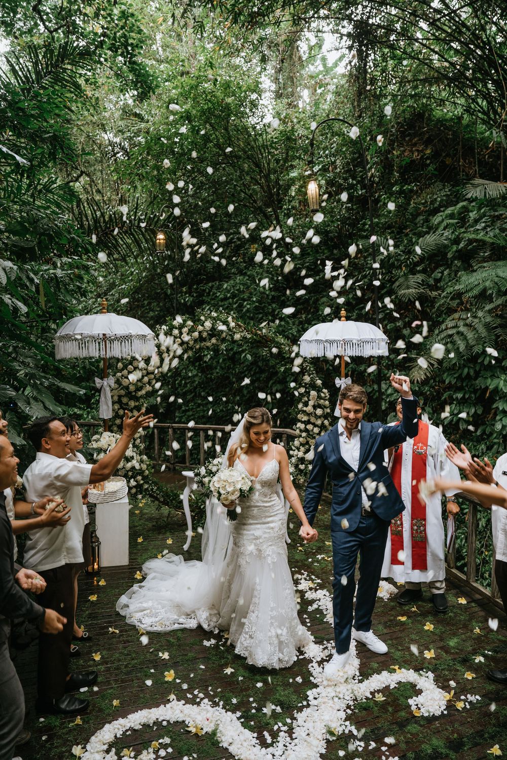 Wedding celebration with flower petals being thrown as couple and guests celebrate under white umbrellas.