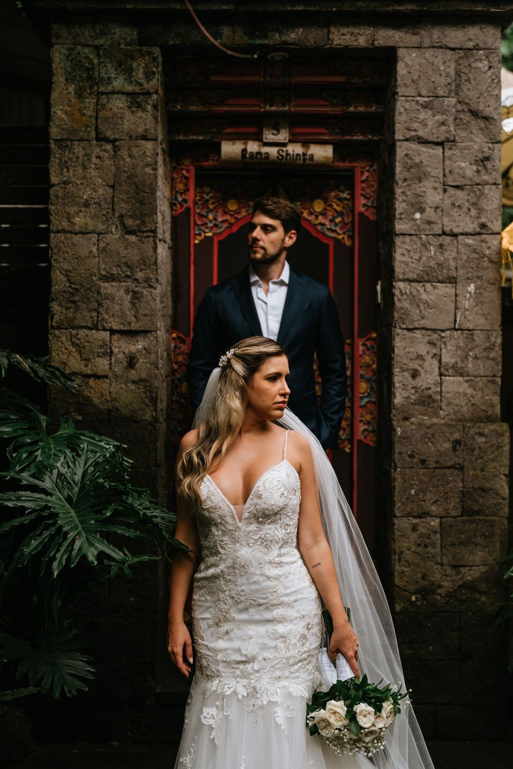Wedding portrait against rustic stone wall with tropical foliage.