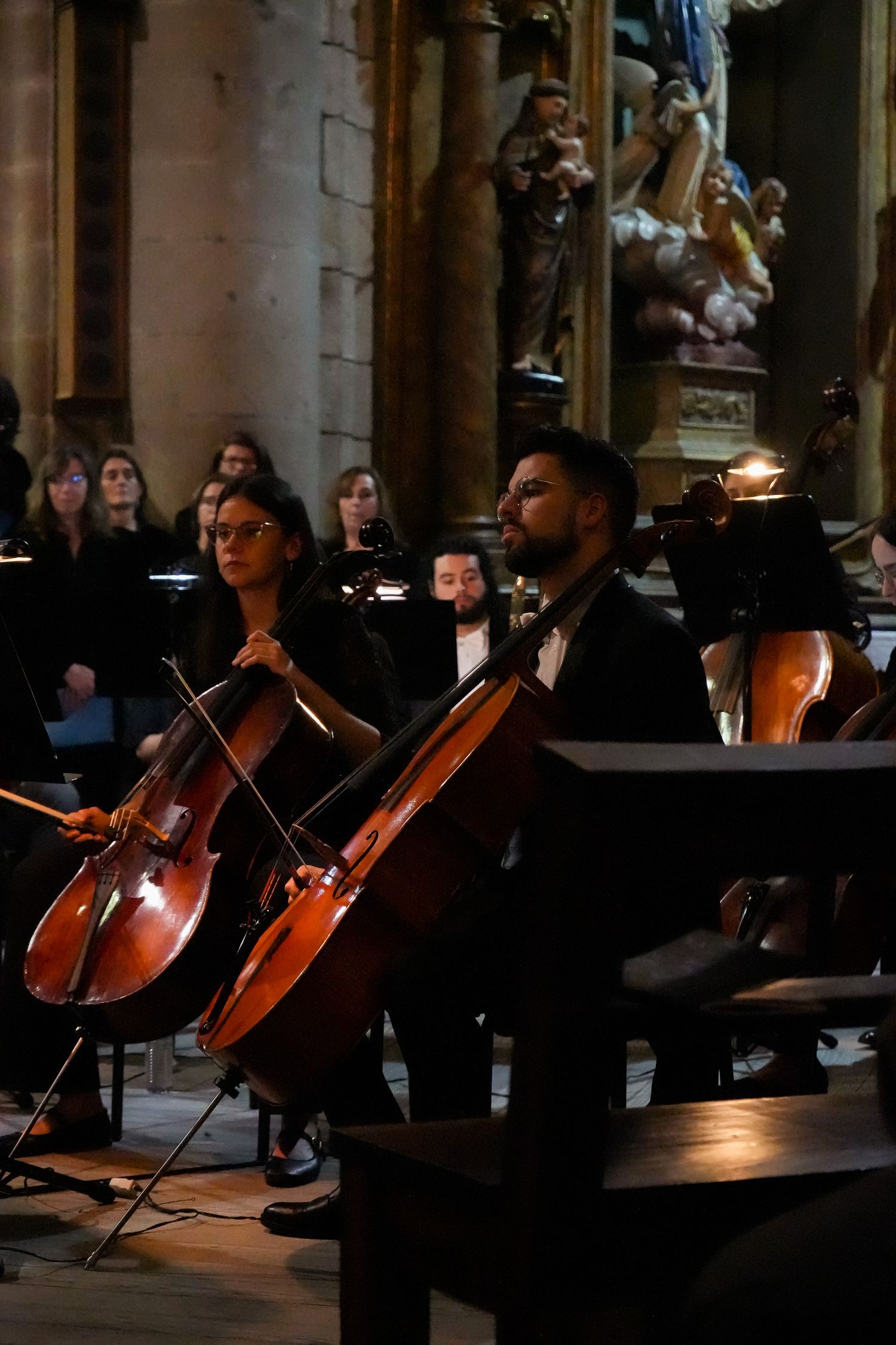 Orchestra cellists performing in a dimly lit cathedral with ornate architectural details.